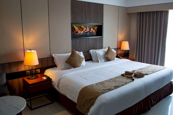 A cozy hotel room with a large bed, two bedside lamps, decorative pillows, a sitting area, and a wall-mounted artwork.