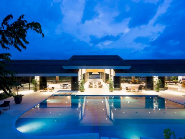 A luxurious resort pool area at dusk, featuring a large pool, lounge chairs, and an open-air building with lights.