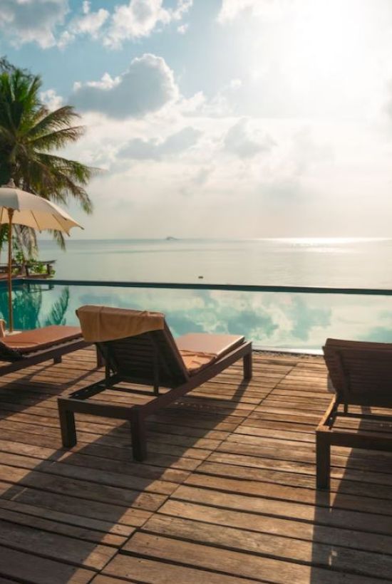 A serene poolside scene with loungers and umbrellas, overlooking a calm sea under a partly cloudy sky.