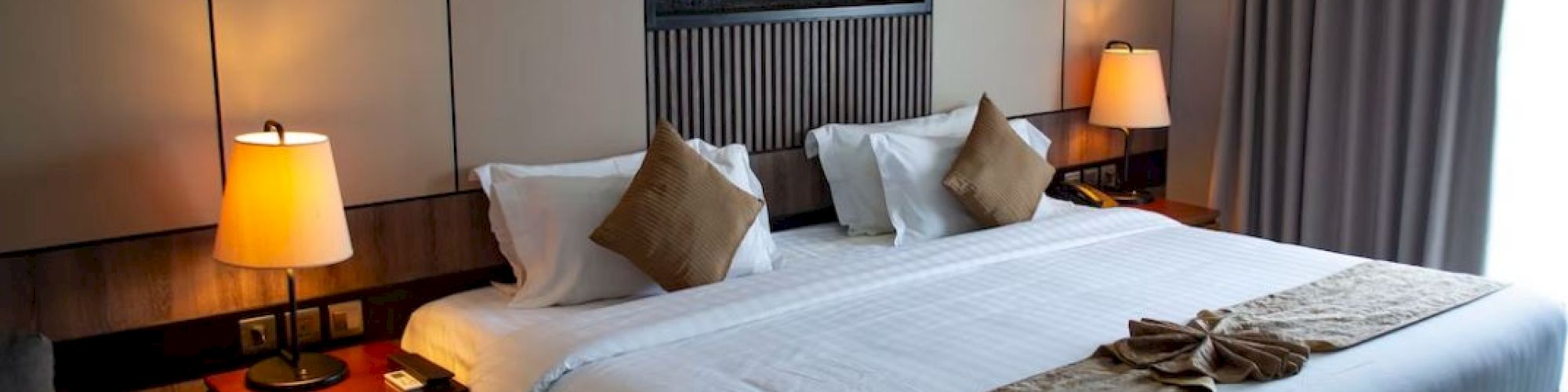 A neatly arranged hotel room with a large bed, two lamps, pillows, and folded towels, featuring a stylish wall decoration.