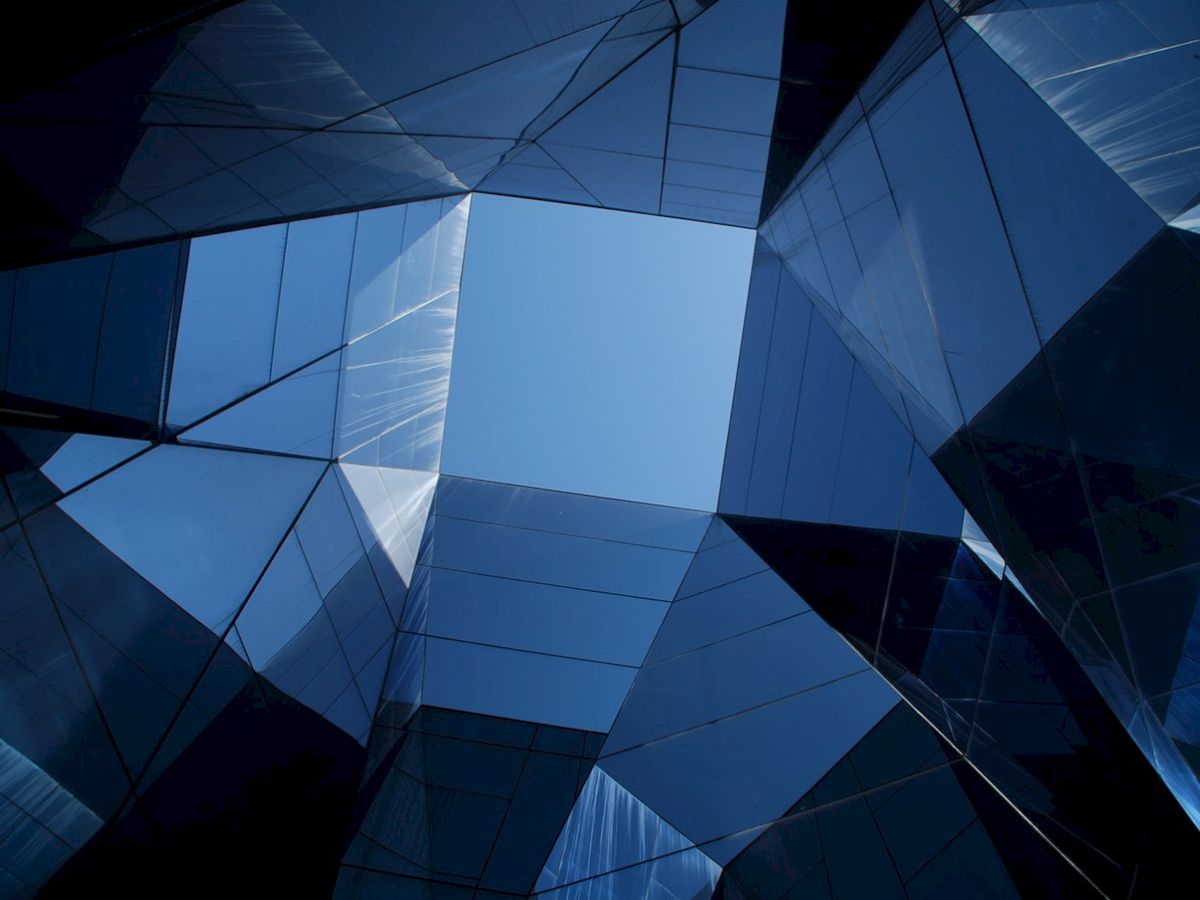 The image shows a geometric pattern of reflective glass surfaces creating an abstract architectural composition against the sky.
