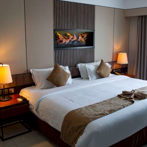 A neatly made hotel room with a large bed, two bedside lamps, a decorative wall piece, and curtains on the right.