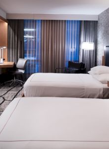 A modern hotel room with two beds, a desk, a TV, and stylish lighting and decor, creating a sleek and inviting atmosphere.