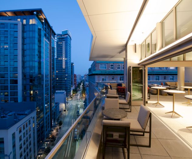 A modern rooftop terrace overlooking a cityscape with illuminated buildings and a stylish seating area on the right side of the image.