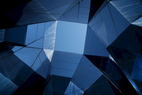 The image shows a geometric pattern formed by skyscrapers reflecting the sky, creating a modern and abstract architectural scene.