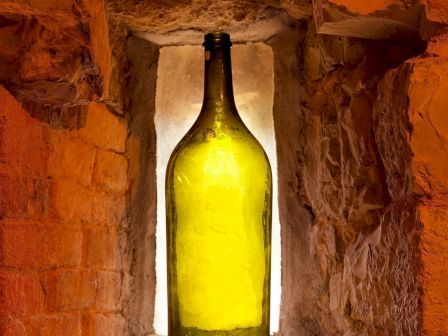 A green bottle is placed in a stone or brick alcove with warm lighting, creating a rustic and cozy atmosphere.