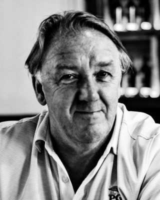 The image shows a black and white portrait of a person with short hair wearing a collared shirt, looking directly at the camera.