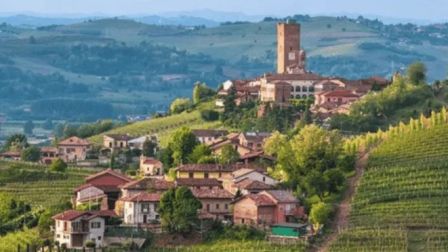 A picturesque hillside village with vineyards, rustic houses, and a tower, set against rolling hills and a serene landscape in the background.