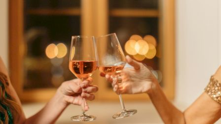 Two people clinking wine glasses in a celebratory toast, with a warm, blurred background of lights.