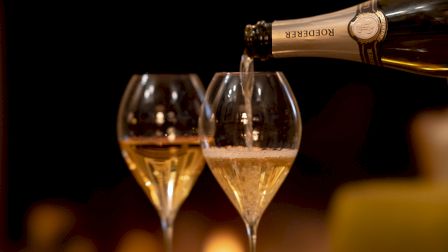 A champagne bottle pours into two fluted glasses, sparkling wine filling the rims with a warm, intimate glow.