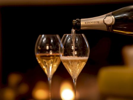 A champagne bottle pours into two fluted glasses, sparkling wine filling the rims with a warm, intimate glow.