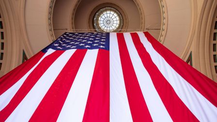 The image shows a large American flag hanging in an archway with a circular window at the top center.