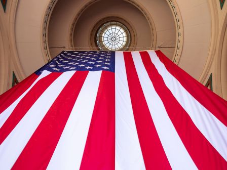 The image shows a large American flag hanging in an archway with a circular window at the top center.