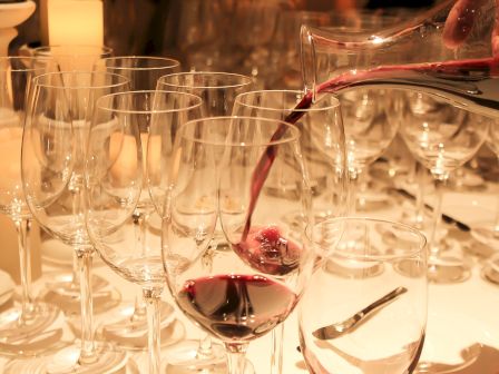 A red wine is being poured into a glass surrounded by empty wine glasses on a table, creating an elegant arrangement.