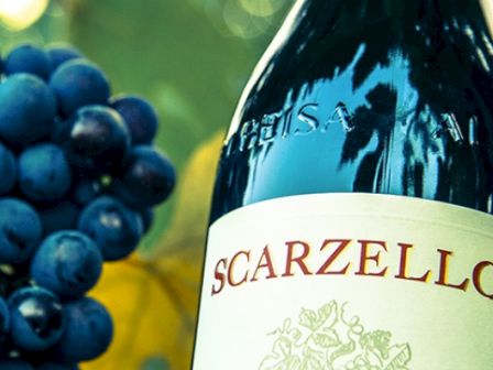 The image shows a bottle of Scarzello wine and a bunch of grapes, against a blurred green background for a wine-related theme.