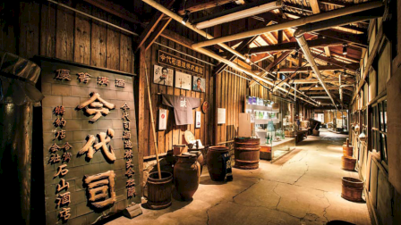 A rustic corridor with wooden barrels, display cases, and Japanese signage under a wooden-beamed roof.