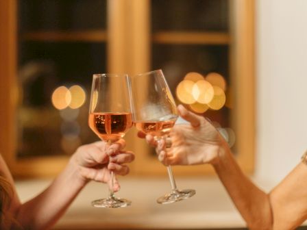 Two people clinking wine glasses in a celebratory toast, with a warm, blurred background of lights.