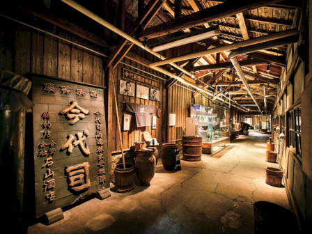 A rustic corridor with wooden barrels, display cases, and Japanese signage under a wooden-beamed roof.