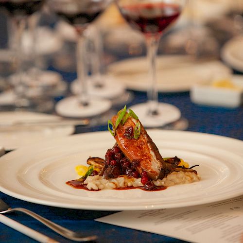 A gourmet plated lamb dish with herbs and sauce, set beside sparkling wine glasses on a dining table.