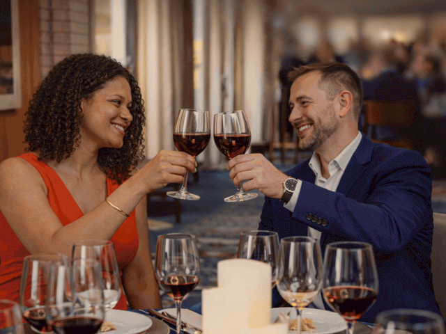 Two people toast with wine glasses at a romantic dinner; smiles, candlelight, and an elegant setting.