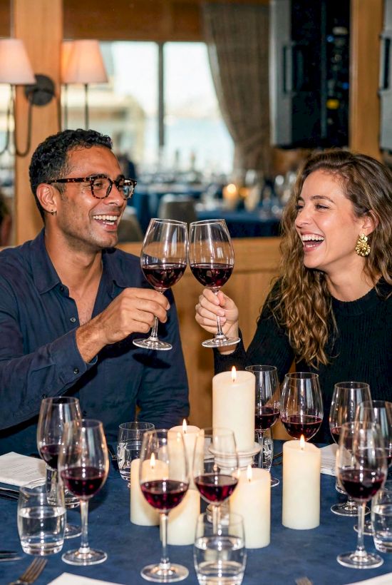 A couple cheers with red wine in glasses at a candlelit dinner, smiling together.