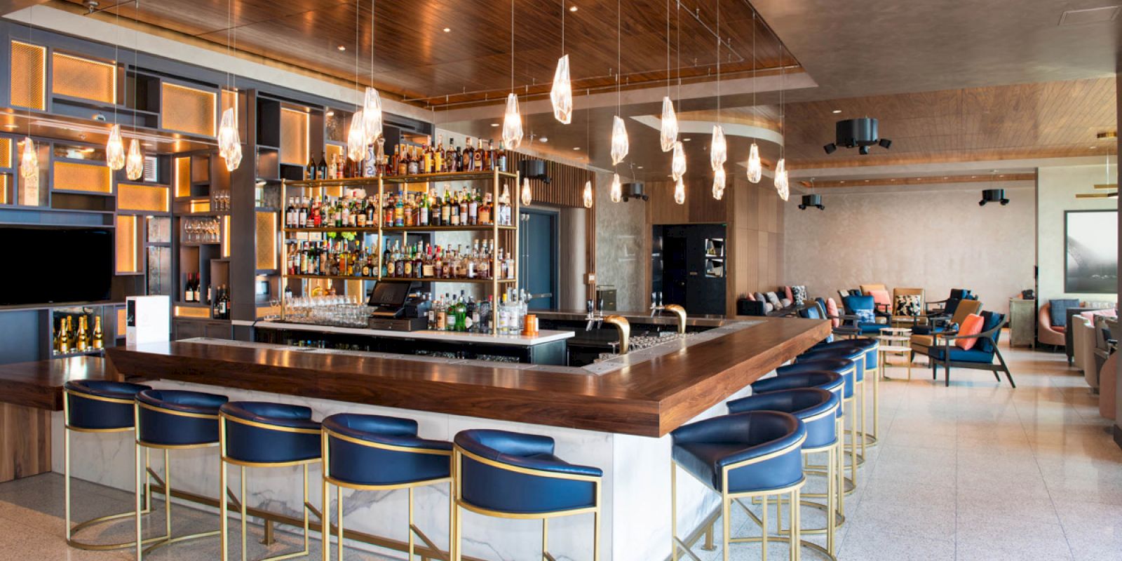 A modern bar with a central counter, stylish bar stools, hanging lights, and a well-stocked selection of bottles in a sleek, open setting.