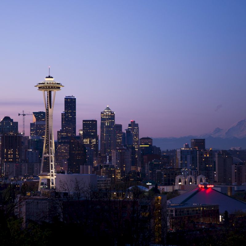 Seattle skyline at dusk with the Space Needle and Mount Rainier in the background under a clear sky.