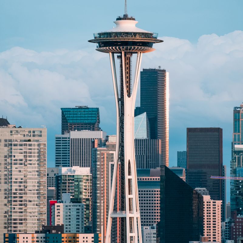 The image shows the Seattle skyline with the Space Needle prominently in the foreground, surrounded by skyscrapers under a cloudy sky.