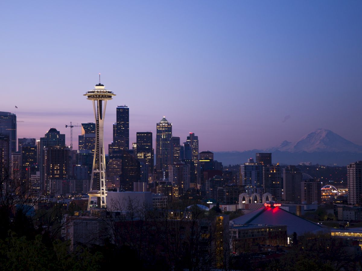 The image shows the Seattle skyline at dusk, featuring the Space Needle, city buildings, and Mount Rainier in the background.