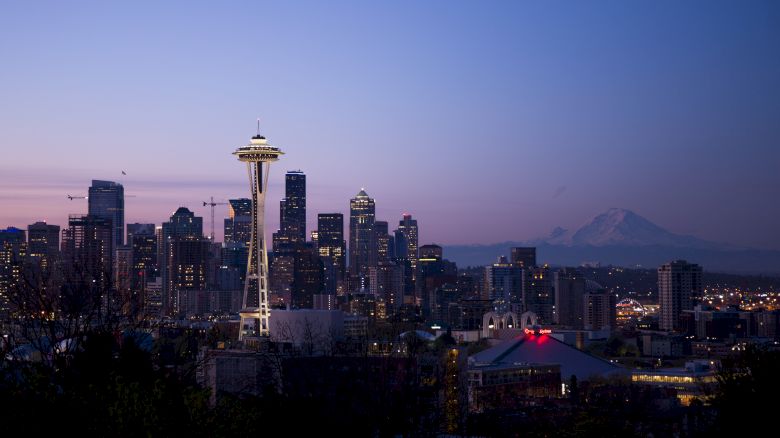 The image shows the Seattle skyline at dusk, featuring the Space Needle, city buildings, and Mount Rainier in the background.