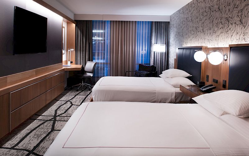 The image shows a modern hotel room with two beds, a flat-screen TV, a desk, and stylish decor ending the sentence.